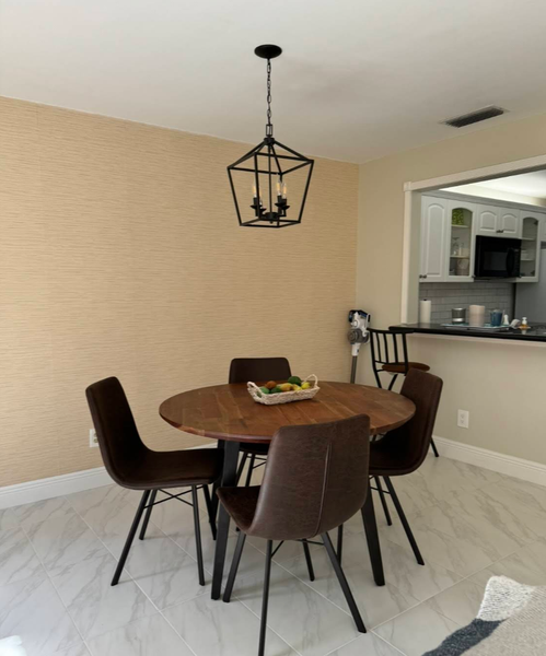Dining room with a round table, four brown chairs, and a black light fixture. Beige wall and white tiled floor.