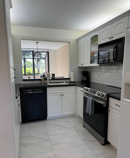 Modern kitchen with white cabinets, black appliances, tile backsplash, and dark countertops.
