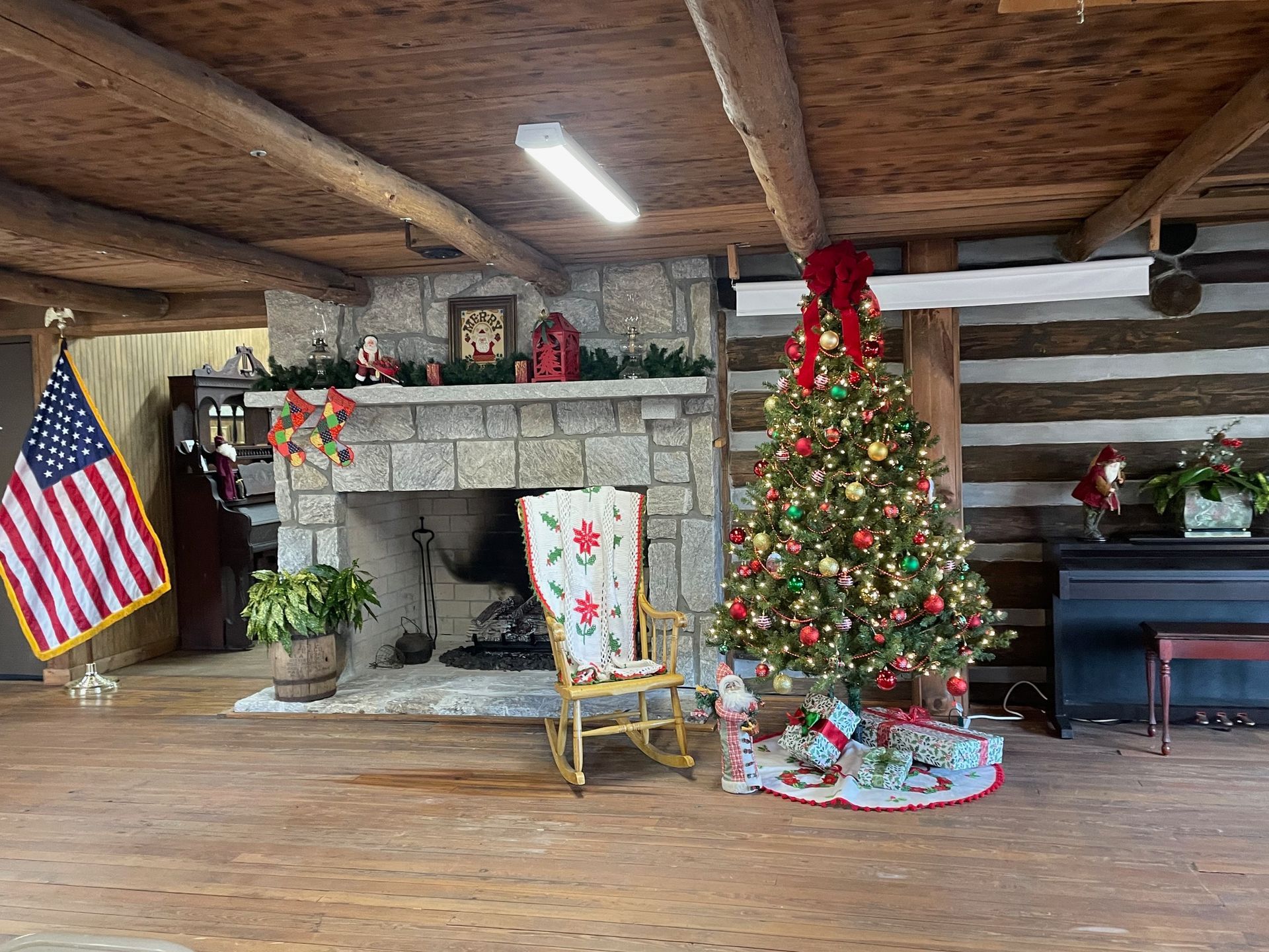 Christmas scene: decorated tree, fireplace, flag, rocking chair in a rustic cabin setting.