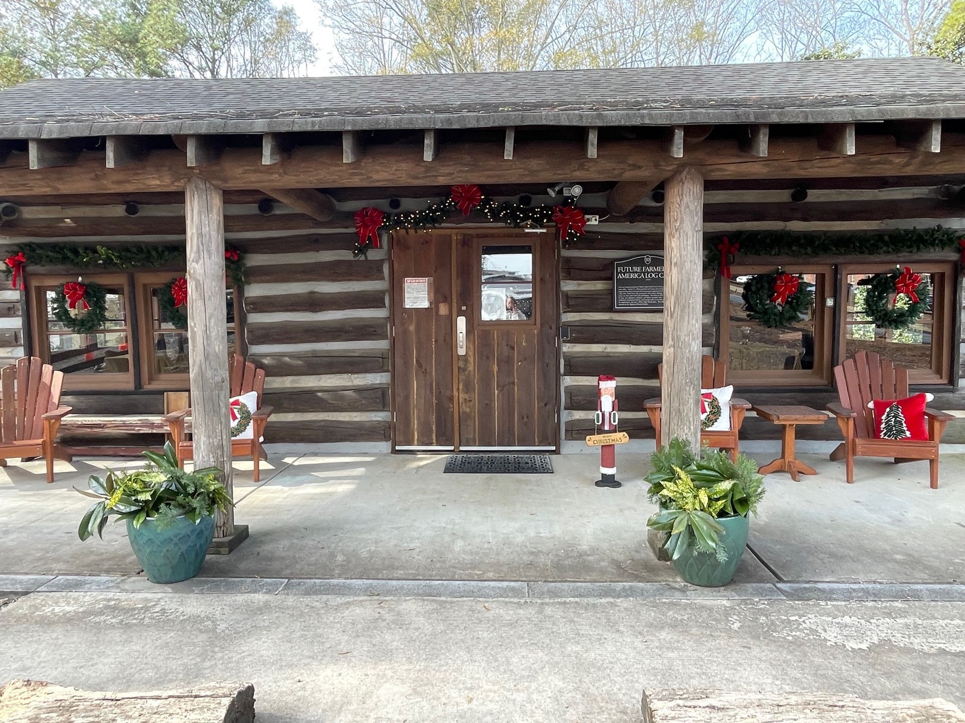Log cabin with Christmas decorations, including wreaths and garland, on a porch with seating.