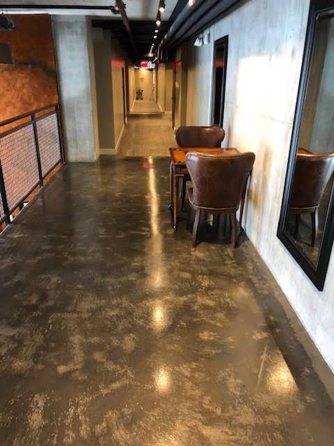 Hallway with polished concrete floor, two chairs and table, long view with doors.