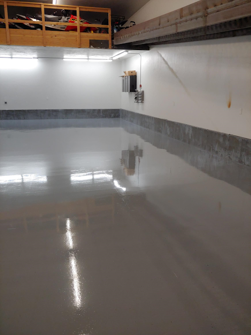 Gray epoxy-coated garage floor with wall reflections, white walls, and a storage cabinet.