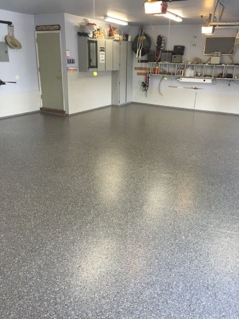A newly coated garage floor with gray flecks, cabinets on the wall, and various tools.