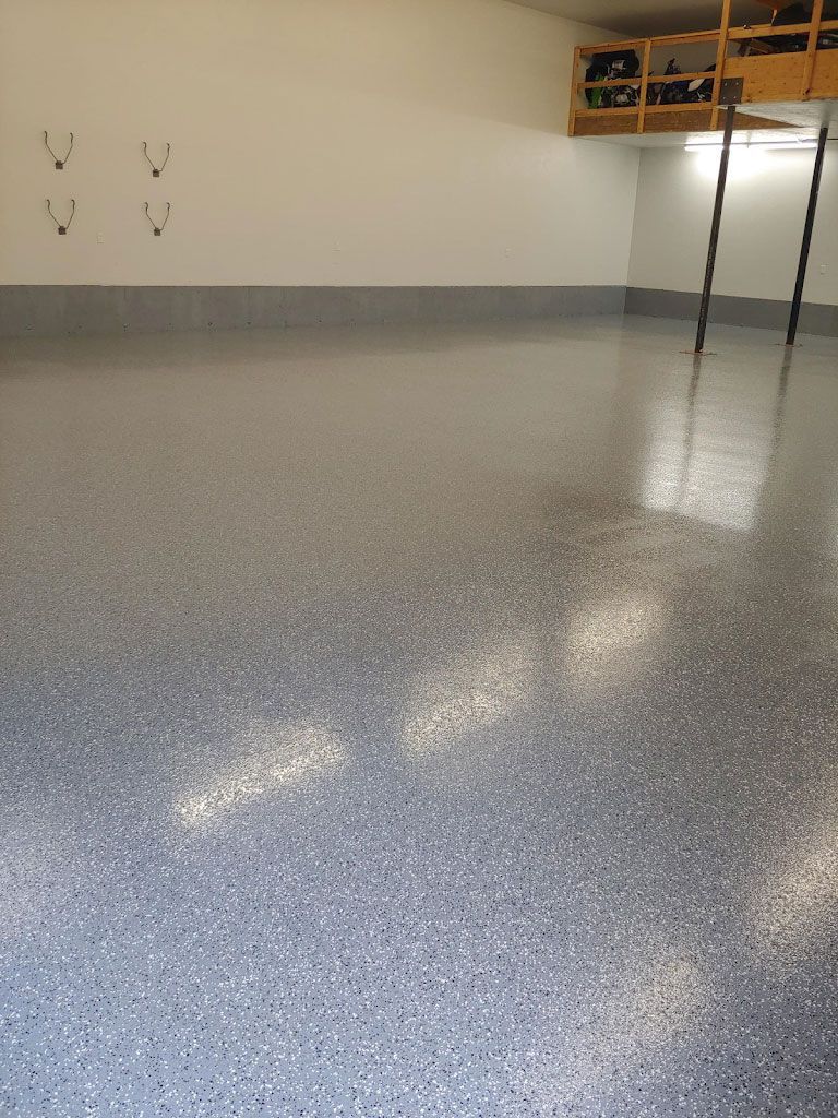 Spacious garage with a speckled gray epoxy floor, white walls, and a shelf unit.