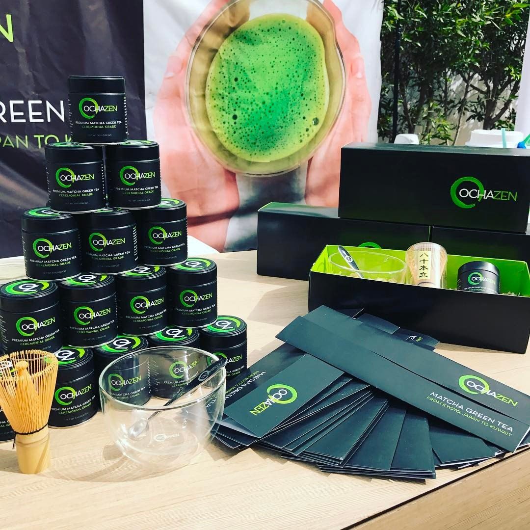 Matcha green tea display: Jars, boxes, whisk, bowls, and promotional materials in a bright setting.