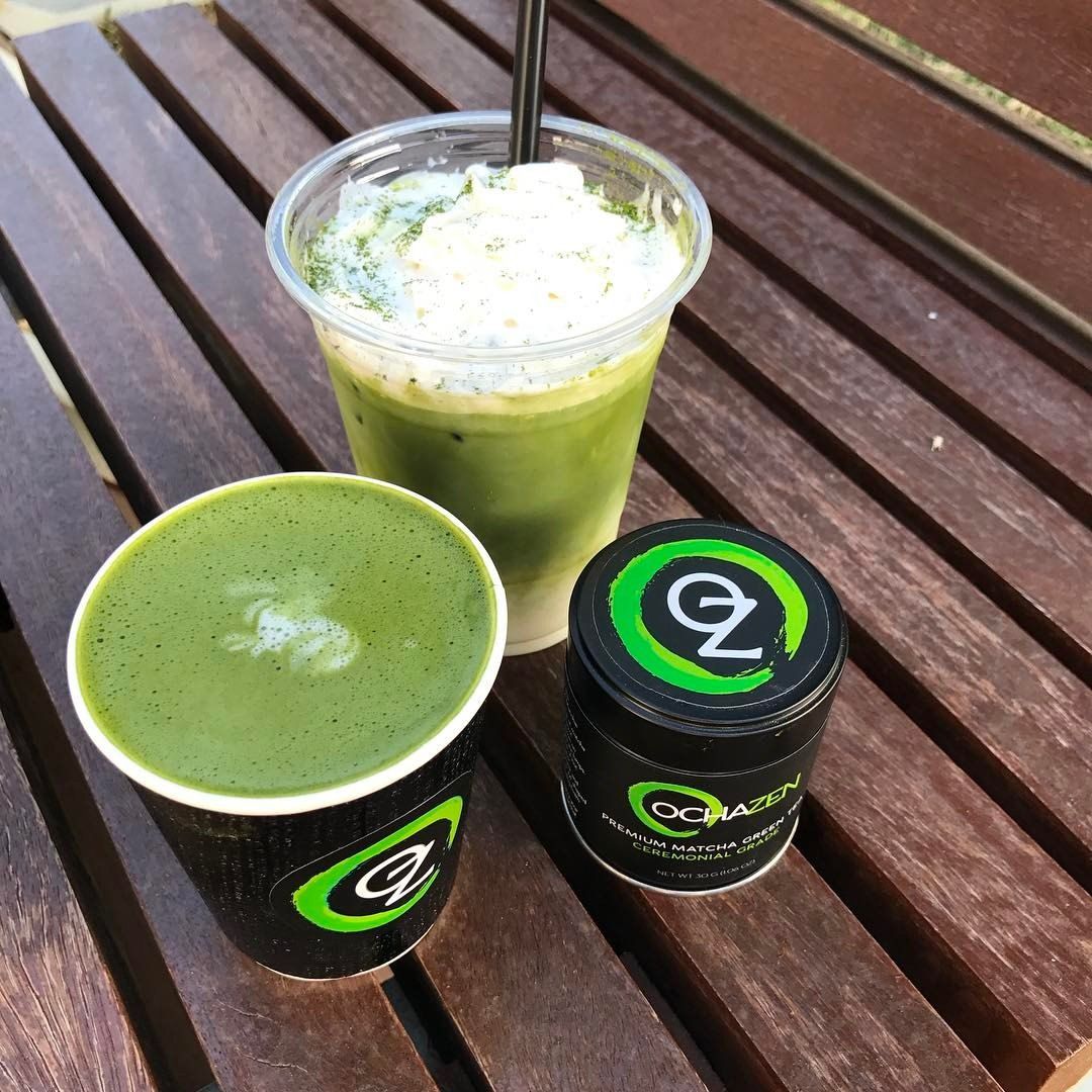 Matcha drinks in two cups and a container on a wooden table.