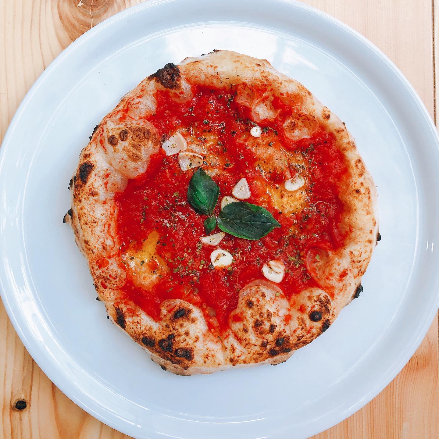 Pizza with tomato sauce, garlic, and basil on a white plate, wood table.