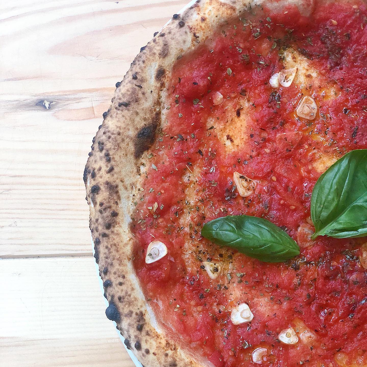 Close-up of a tomato pizza with garlic and basil, on a light wood surface.