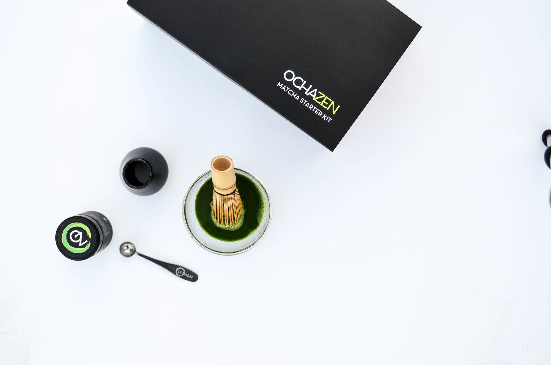 Matcha preparation kit: green powder, whisk, bowl, and accessories on white background.