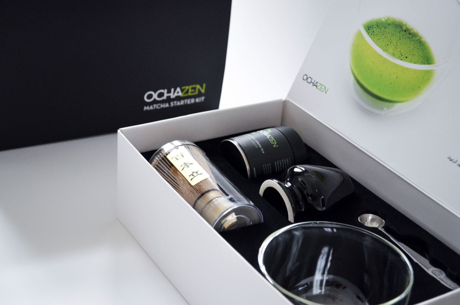 Open matcha starter kit with matcha powder, whisk, bowl, and spoon in a black and white box.