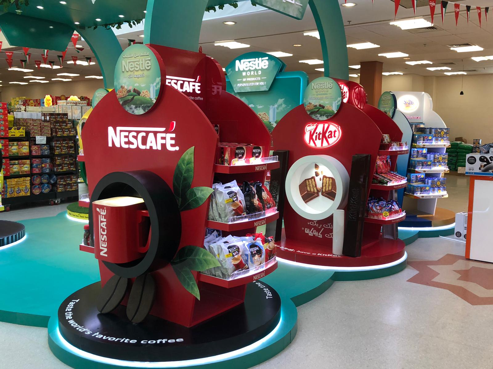 Display of Nestlé products in a store, including Nescafe and Kit Kat, on red circular shelves with green accents.