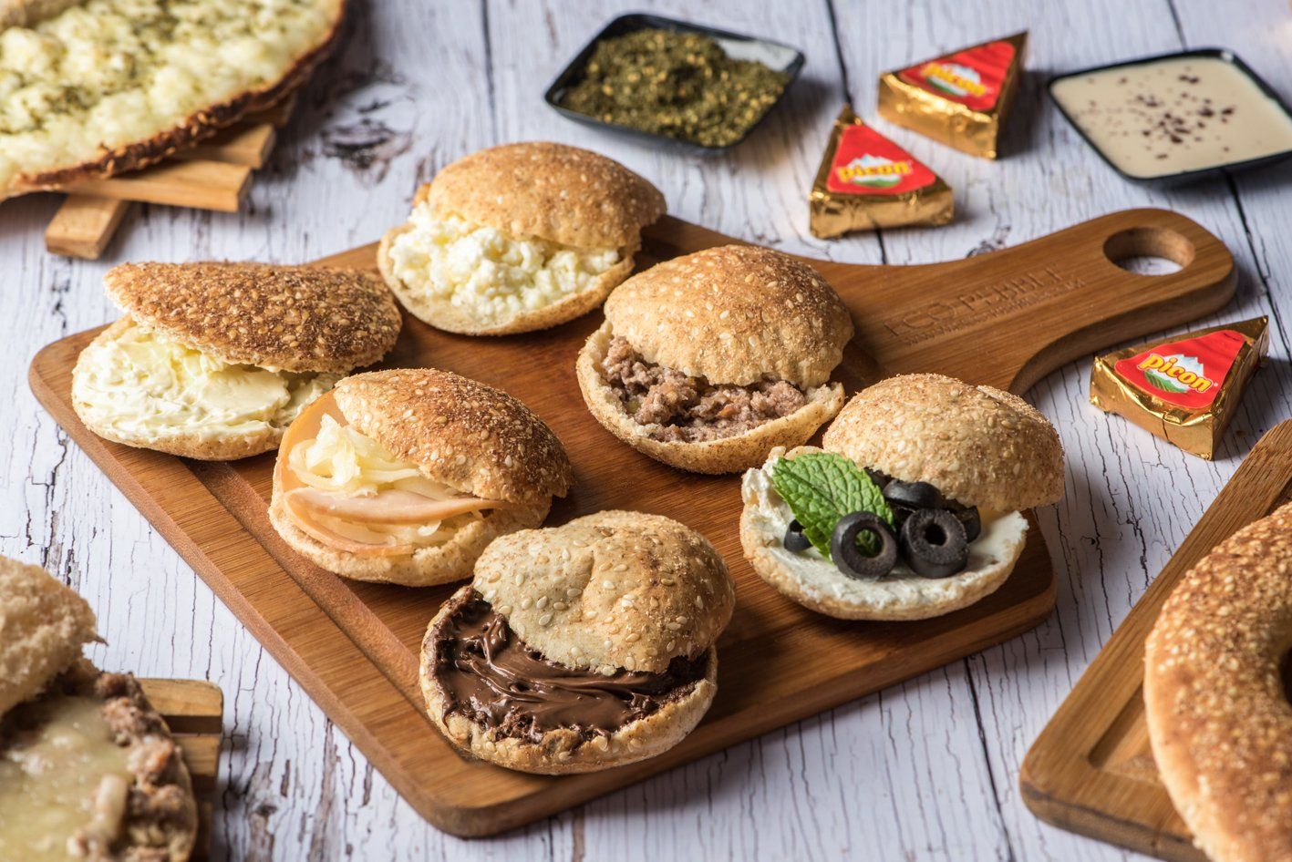 Small sandwiches with various fillings on wooden boards, alongside sauces and a flatbread.