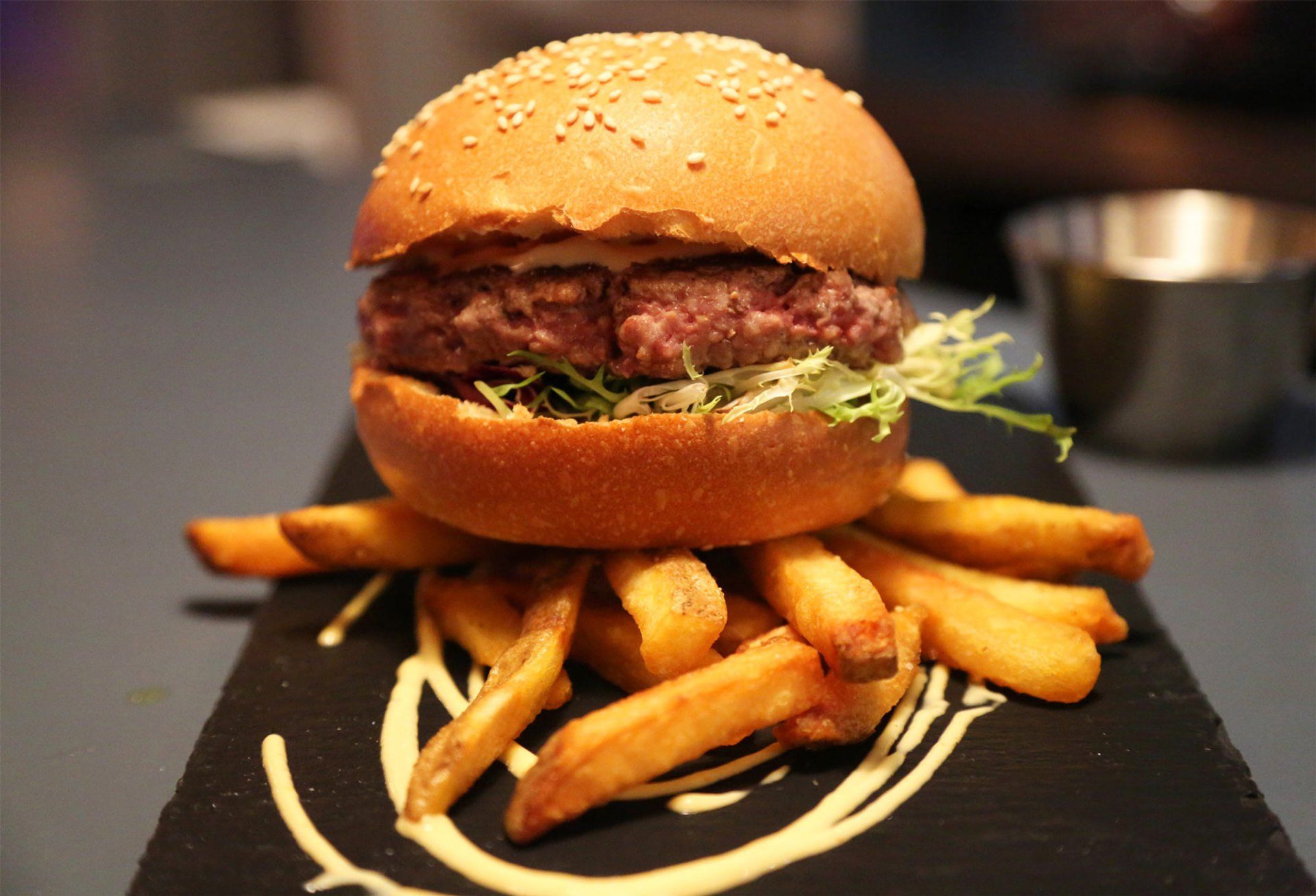 Burger on a bed of fries, served on a black slate.