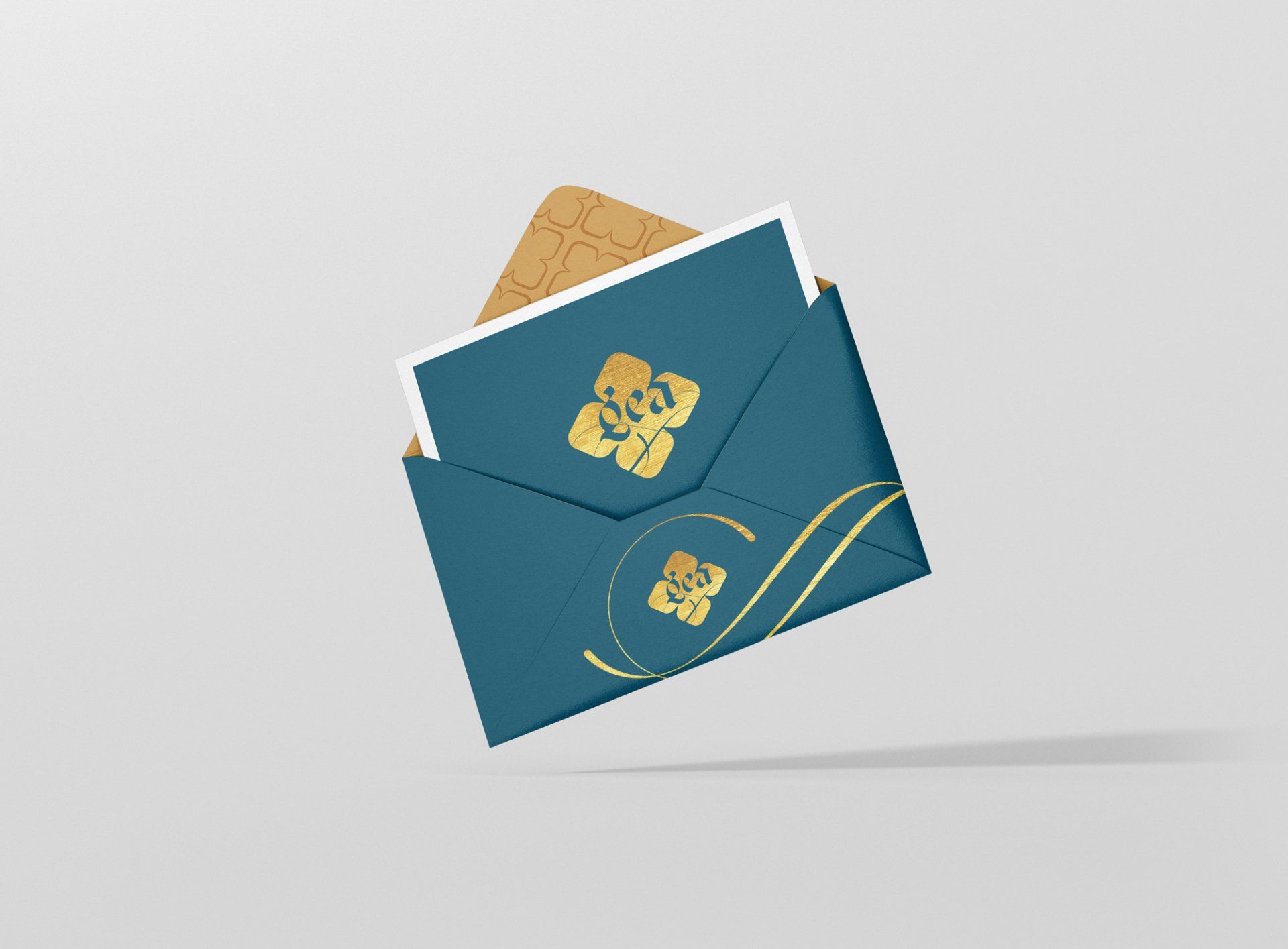 Teal envelope with gold floral design, holding a card on a white background.