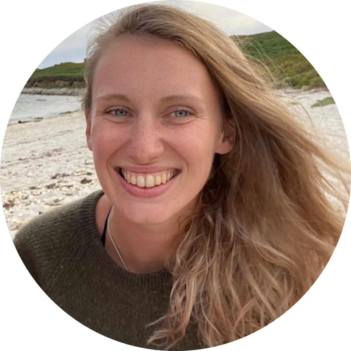 Woman with blonde hair smiling on a beach.