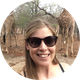 Woman smiling with giraffes in a natural setting, wearing sunglasses.