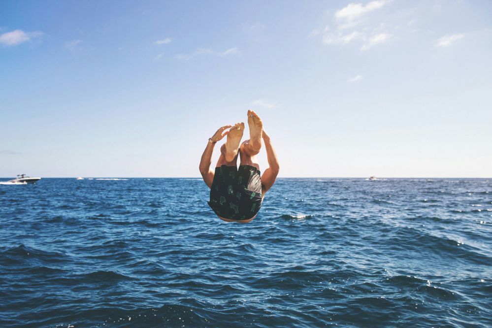 Person doing a backflip into the ocean on a sunny day.