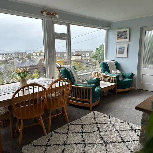 Living room with green armchairs, wooden table, and large window overlooking a town.