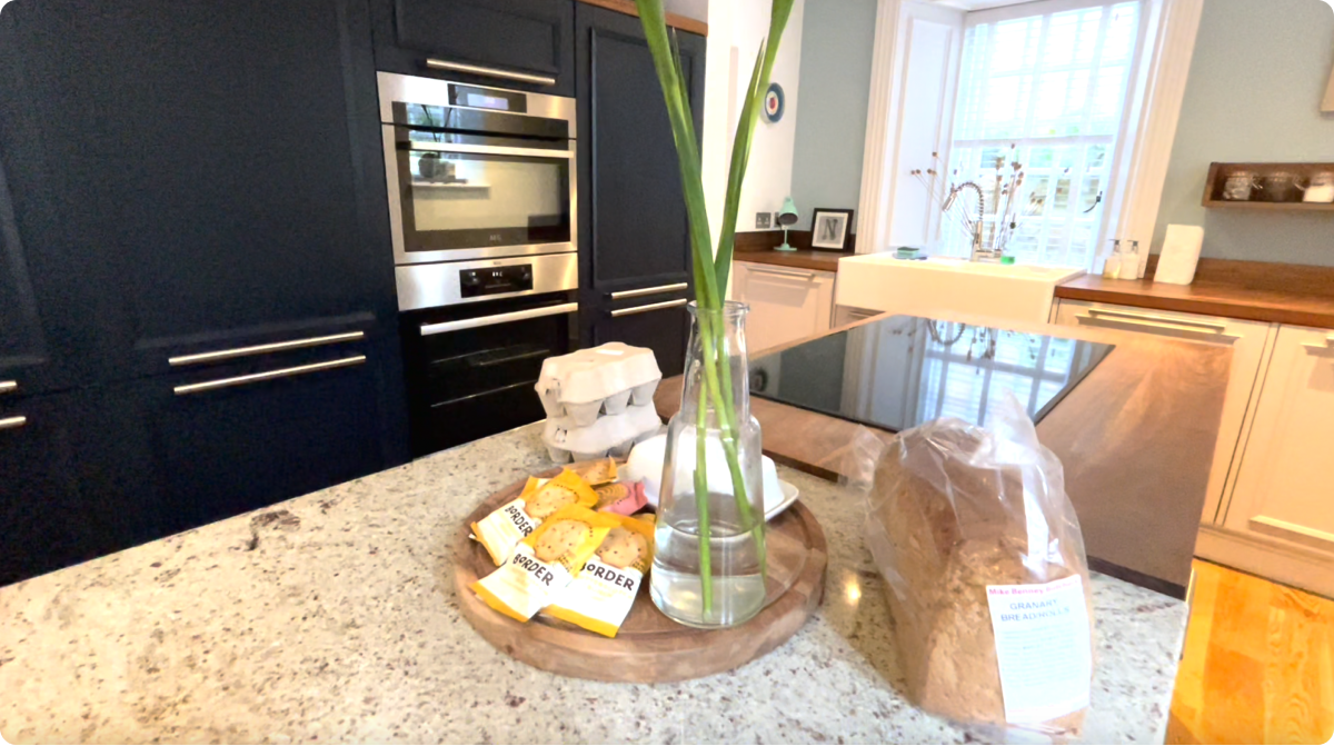 Kitchen with blue cabinets, granite countertops, and a wooden island. A vase of flowers, bread, and snacks on the island.