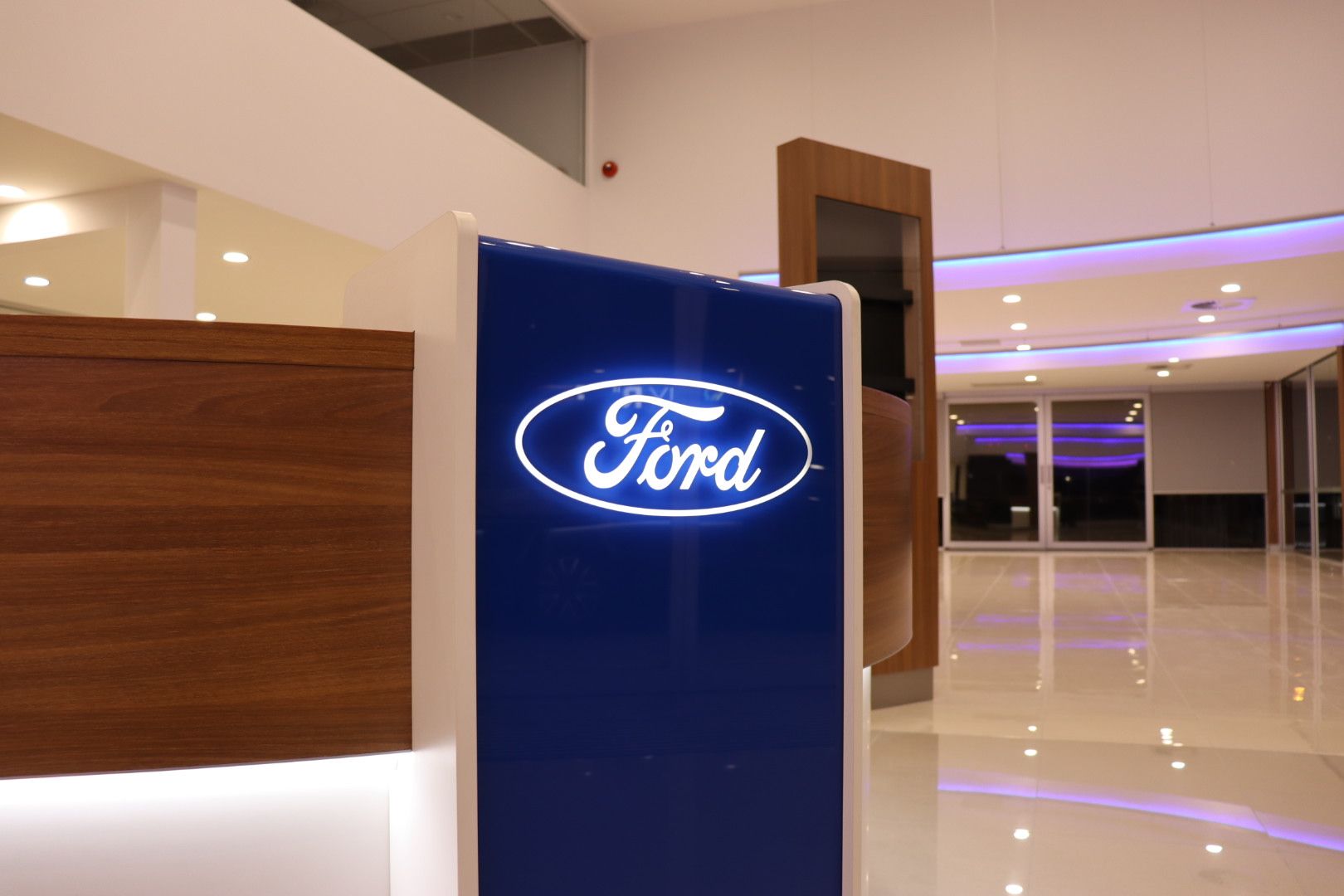 A glowing, blue Ford logo sign stands on a desk in a modern, brightly lit car dealership showroom — Hspark Electrical PTY LTD in Appin, NSW