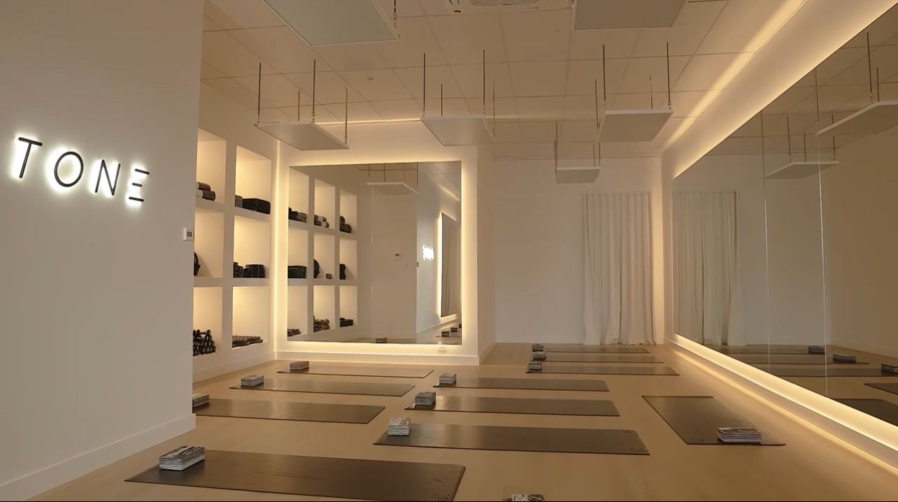 A bright, minimalist studio with yoga mats laid out on a light wood floor and a neon 