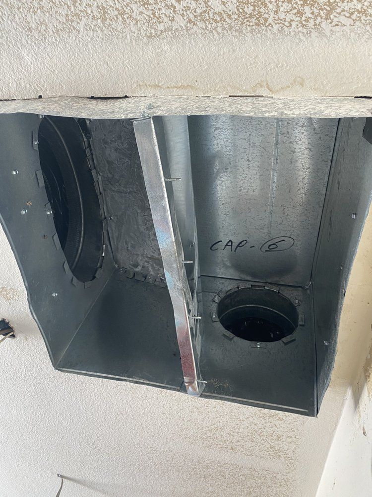 Metal ductwork box attached to a ceiling, with a central support and circular openings for airflow.
