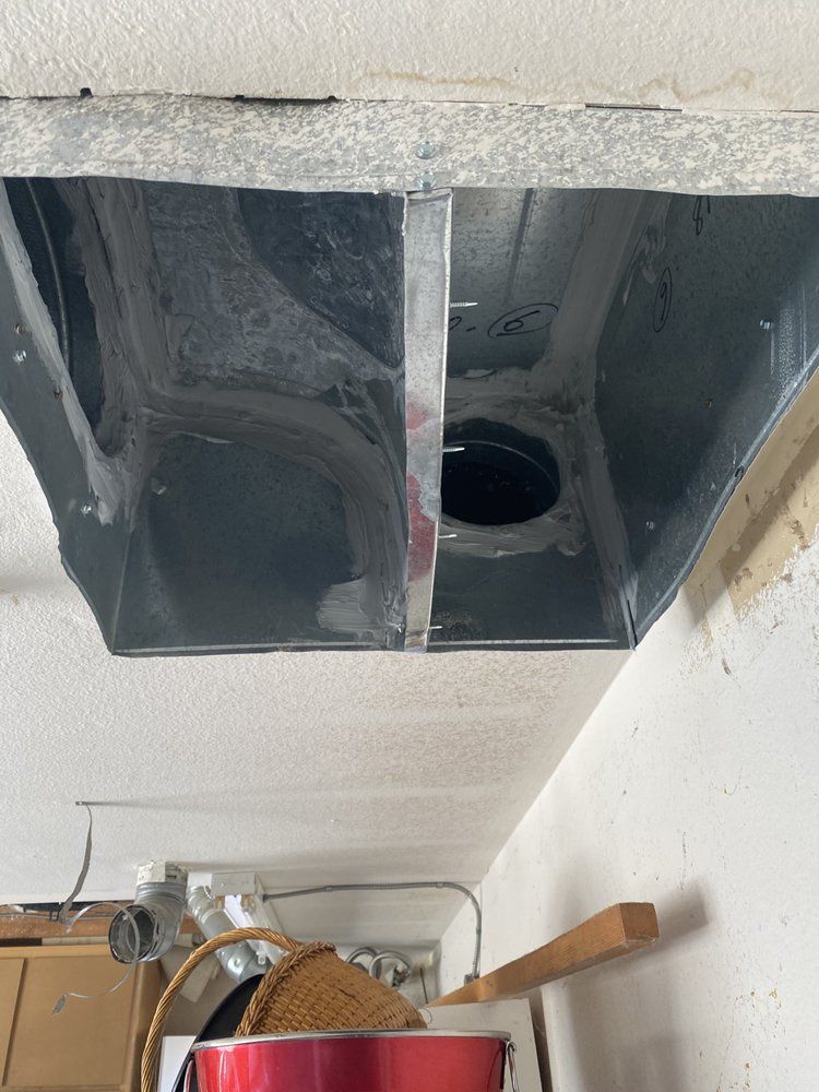 A rectangular metal duct opening in a ceiling, with a round hole visible inside. Gray with light ceiling.