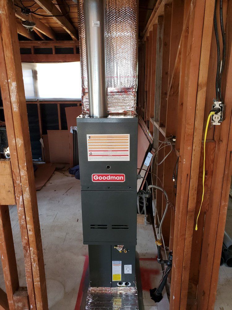 A Goodman furnace installed between wooden studs; a metal chimney pipe leads upwards.