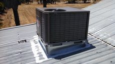 Air conditioning unit installed on a corrugated metal roof. The unit is gray. Outside in sunlight.