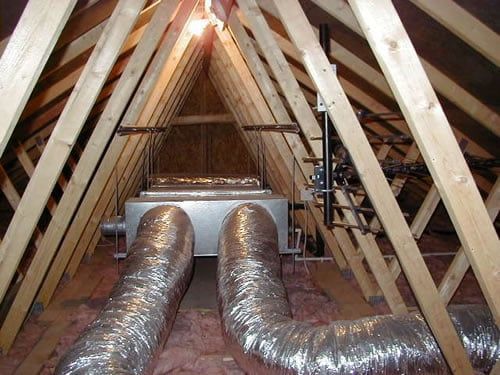 HVAC system in attic with silver ducts, centered between wooden rafters, light shining.