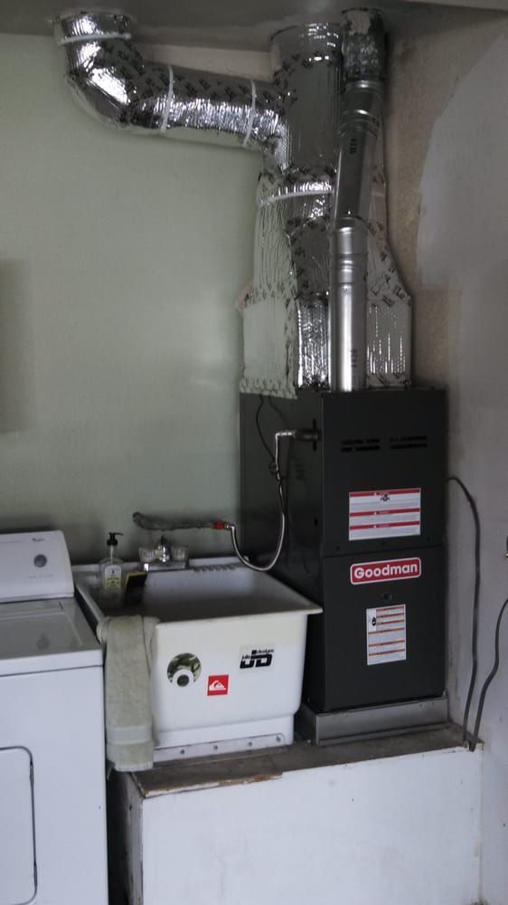 Furnace unit with ductwork, laundry sink, and washing machine in a utility room.
