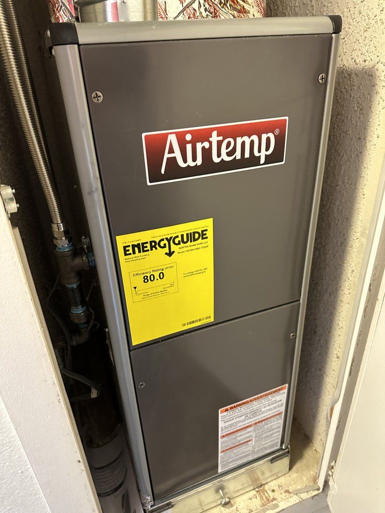 Airtemp furnace unit with Energy Guide sticker, in a utility closet. Gray with black trim.