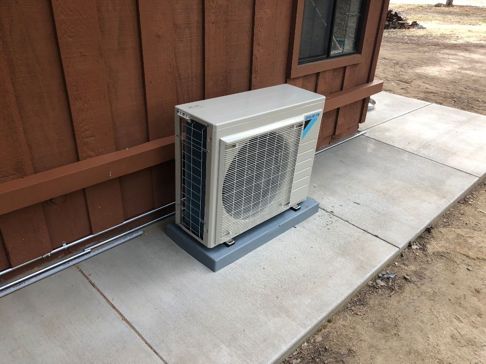 Air conditioning unit on a concrete pad next to a brown building.