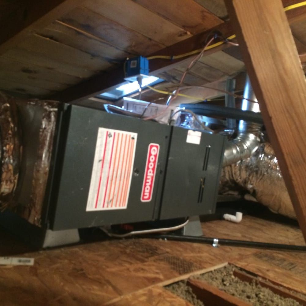 HVAC unit in an attic. A Goodman unit is installed in an attic with ductwork, wooden beams, and insulation.