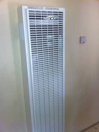 White wall-mounted heater with a louvered front on a light-colored wall, next to a small thermostat.