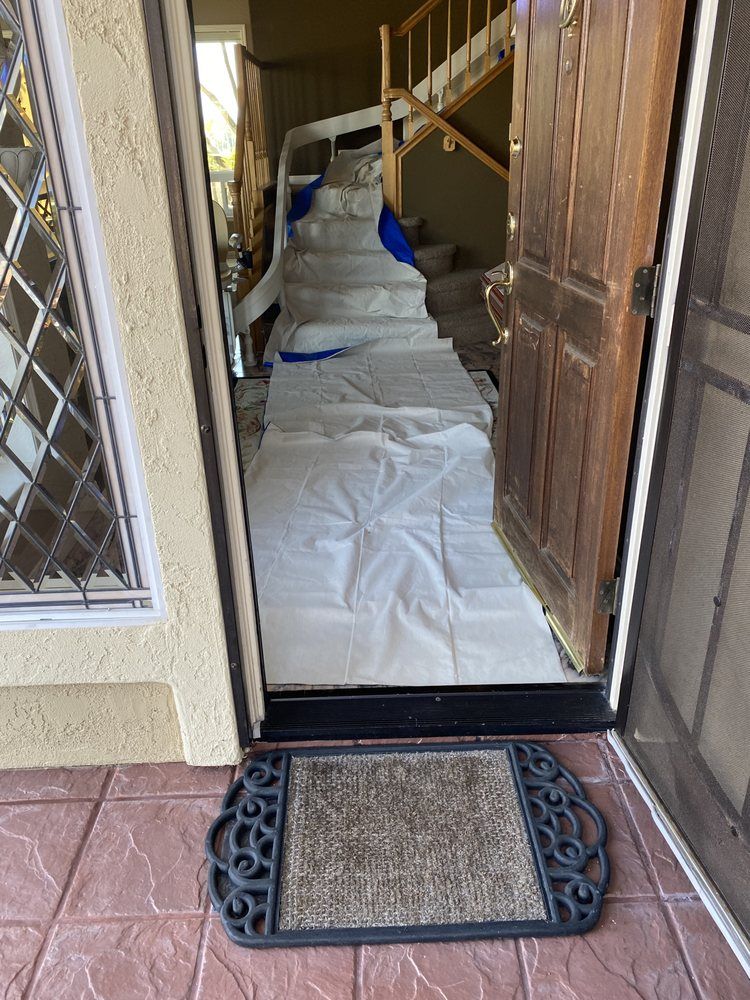 Open doorway with steps covered in protective sheeting. Doormat in foreground.
