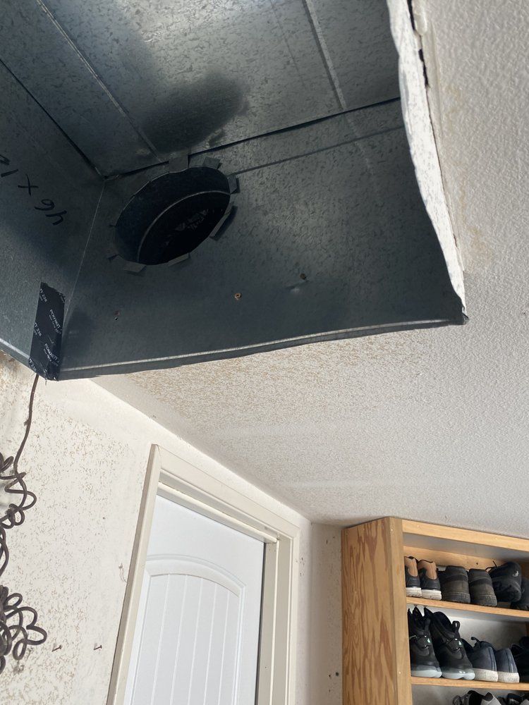 Metal ductwork with a circular opening, mounted in a ceiling next to a white door and wood cabinet.