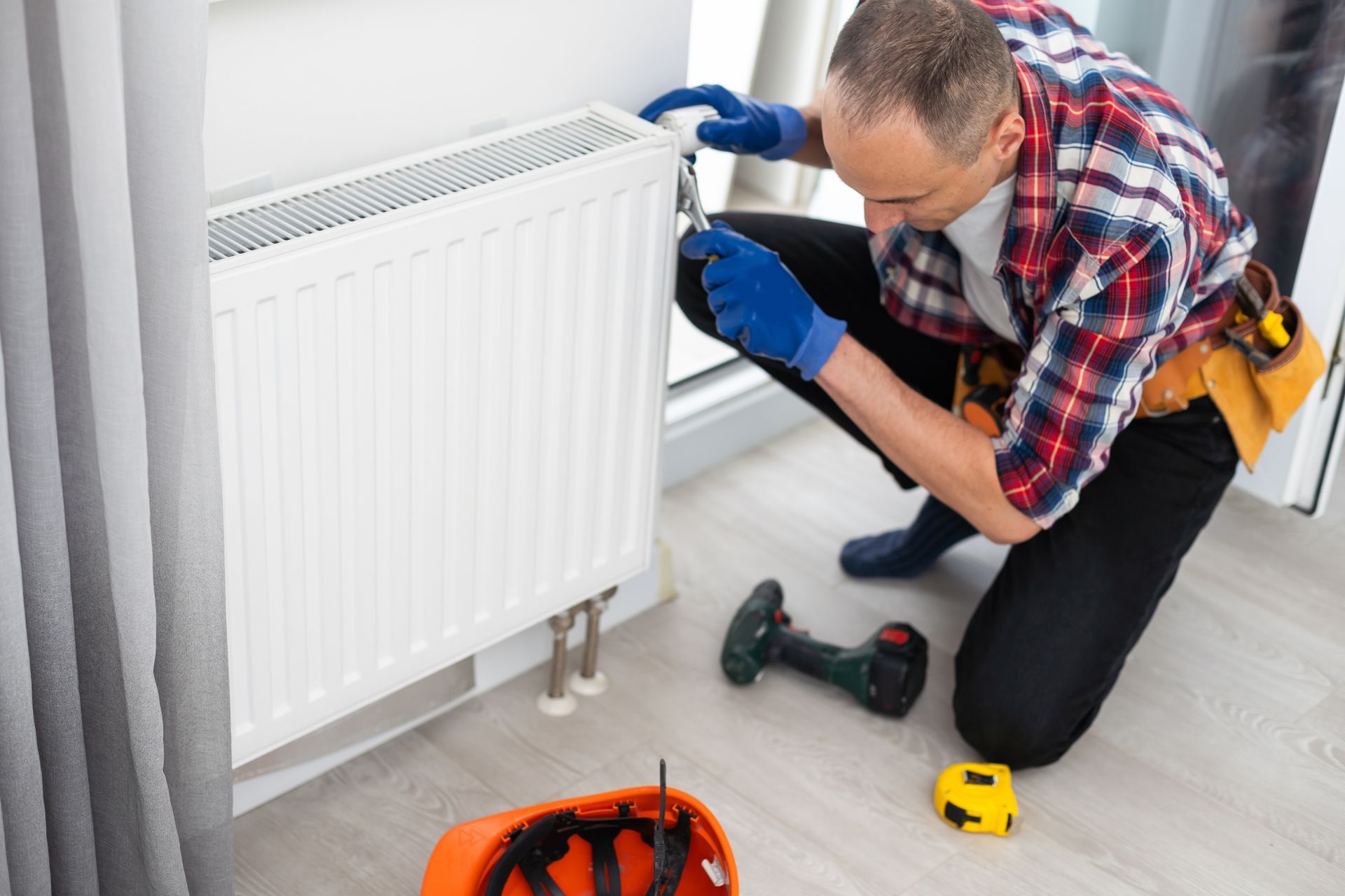Person in work clothes repairing a radiator with a drill and tools.