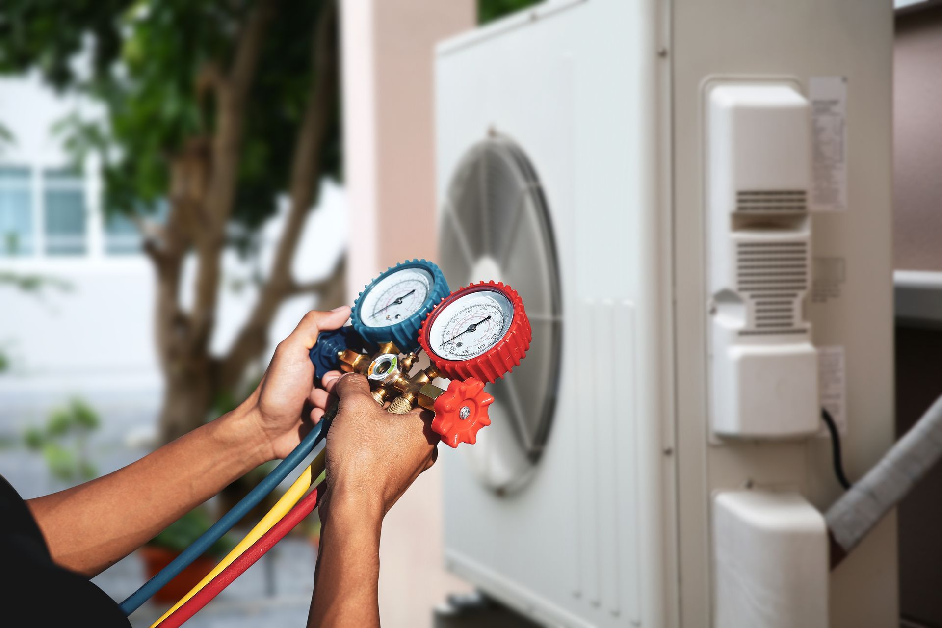Person using gauges to check an outdoor air conditioning unit.