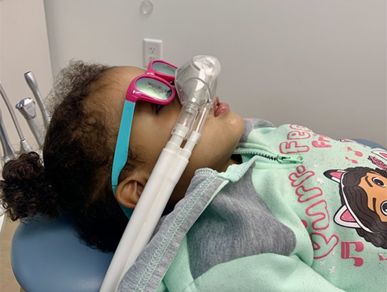 A young boy is laying in a dental chair with an oxygen mask on his face.