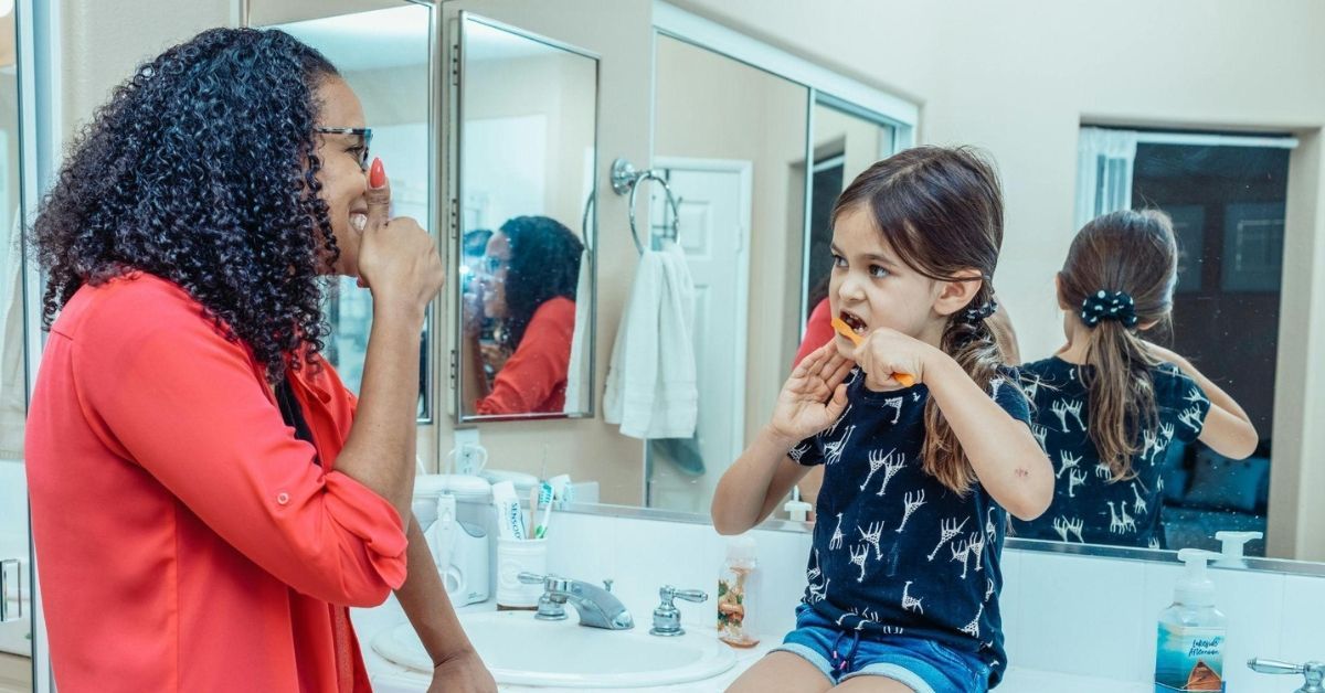 Caregiver helping child brush teeth with charcoal toothpaste at home 