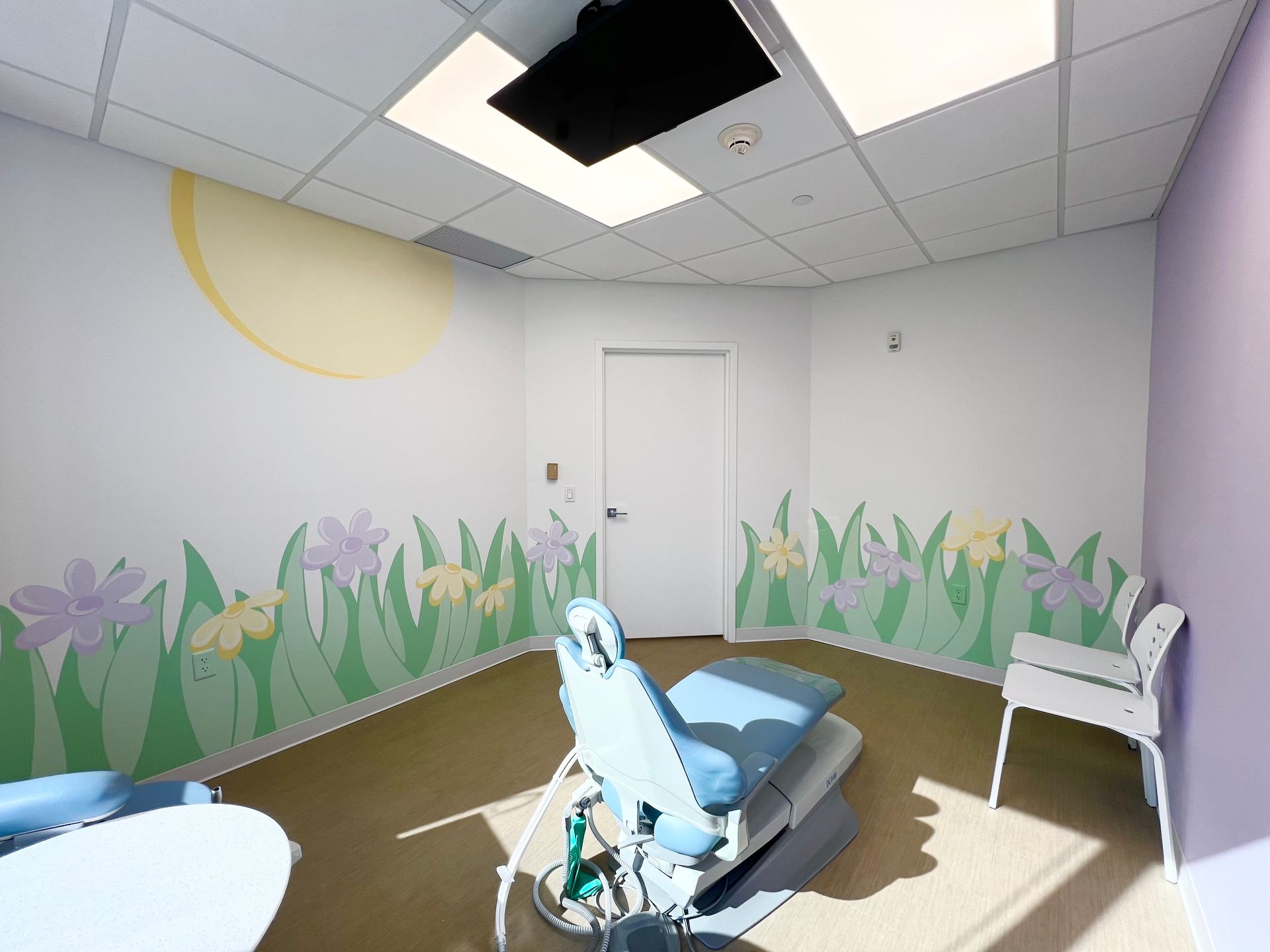 Pediatric dentist office in Nyack with a child-friendly treatment room, dental chair, and bright wall art featuring flowers and sunshine.
