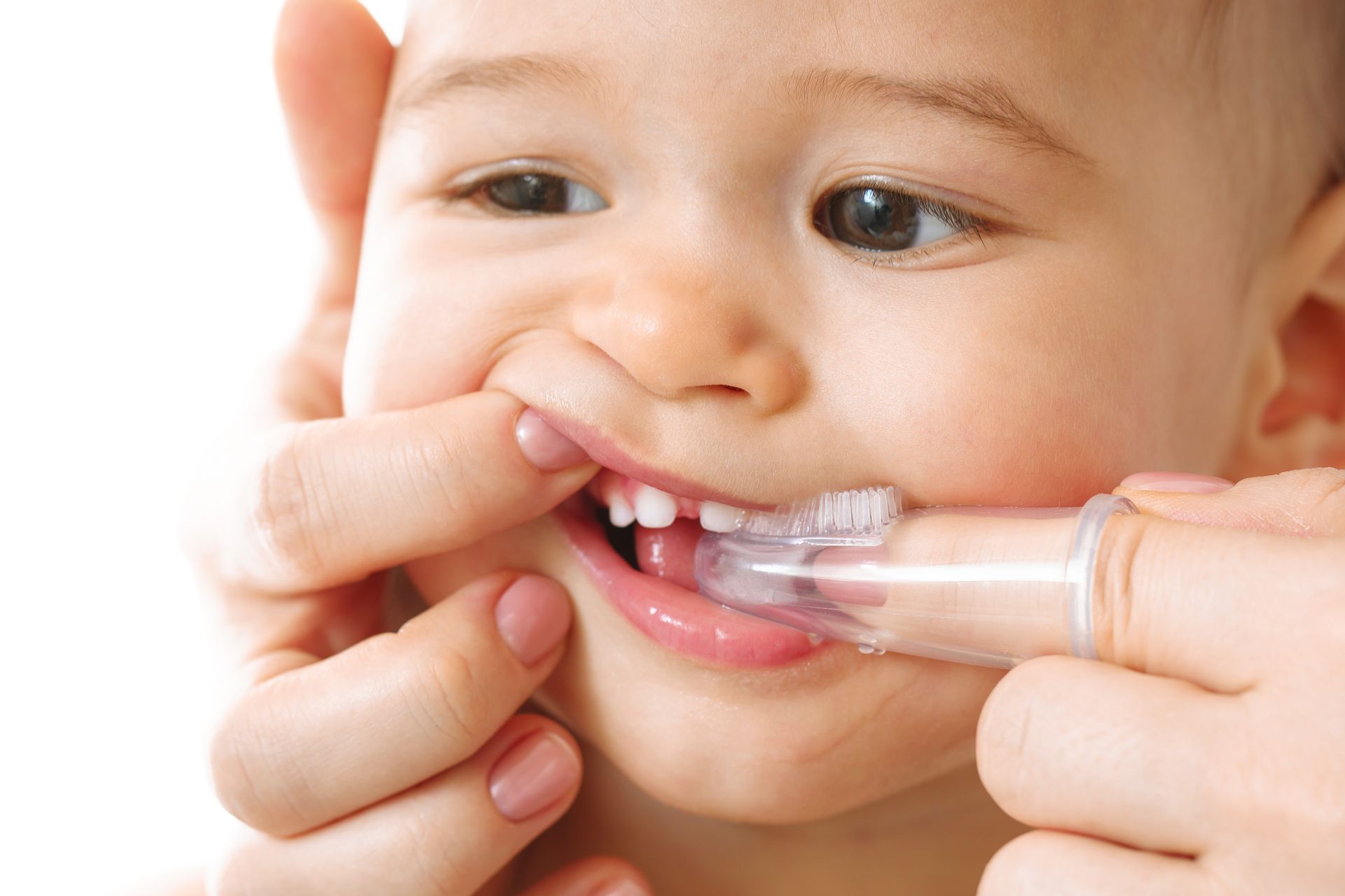 A woman is brushing a baby 's teeth with a finger toothbrush.