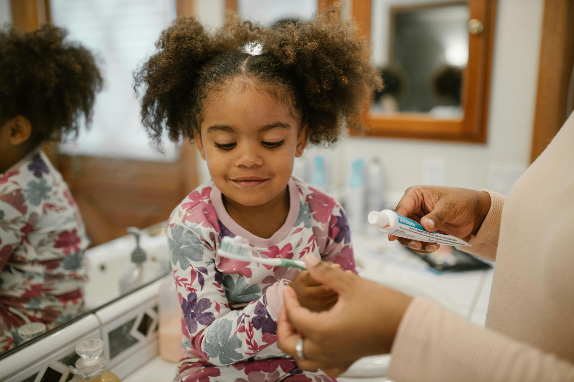 A woman is putting toothpaste on a child 's toothbrush in a bathroom.