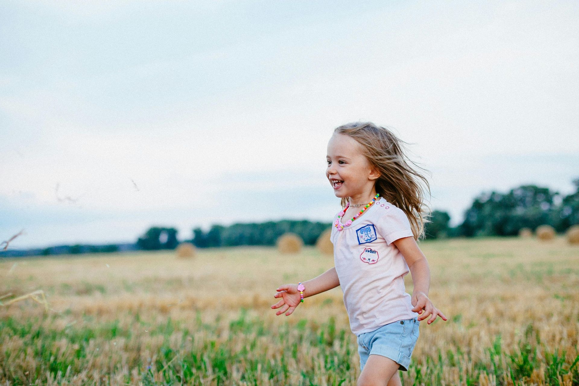 A little girl is running through a field of hay.