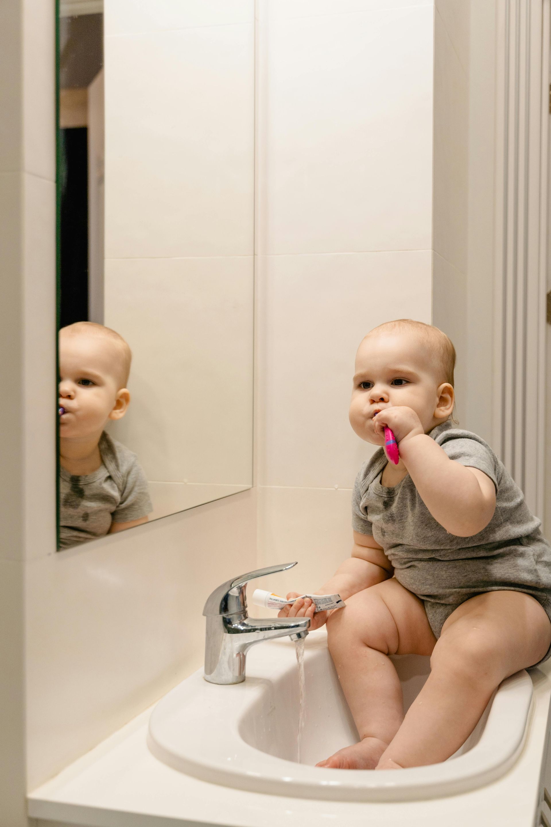 A baby is brushing his teeth in a bathroom sink.