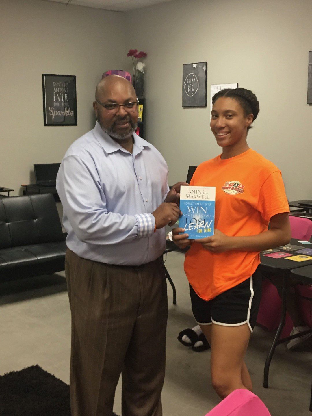 A man is giving a book to a girl in an orange shirt