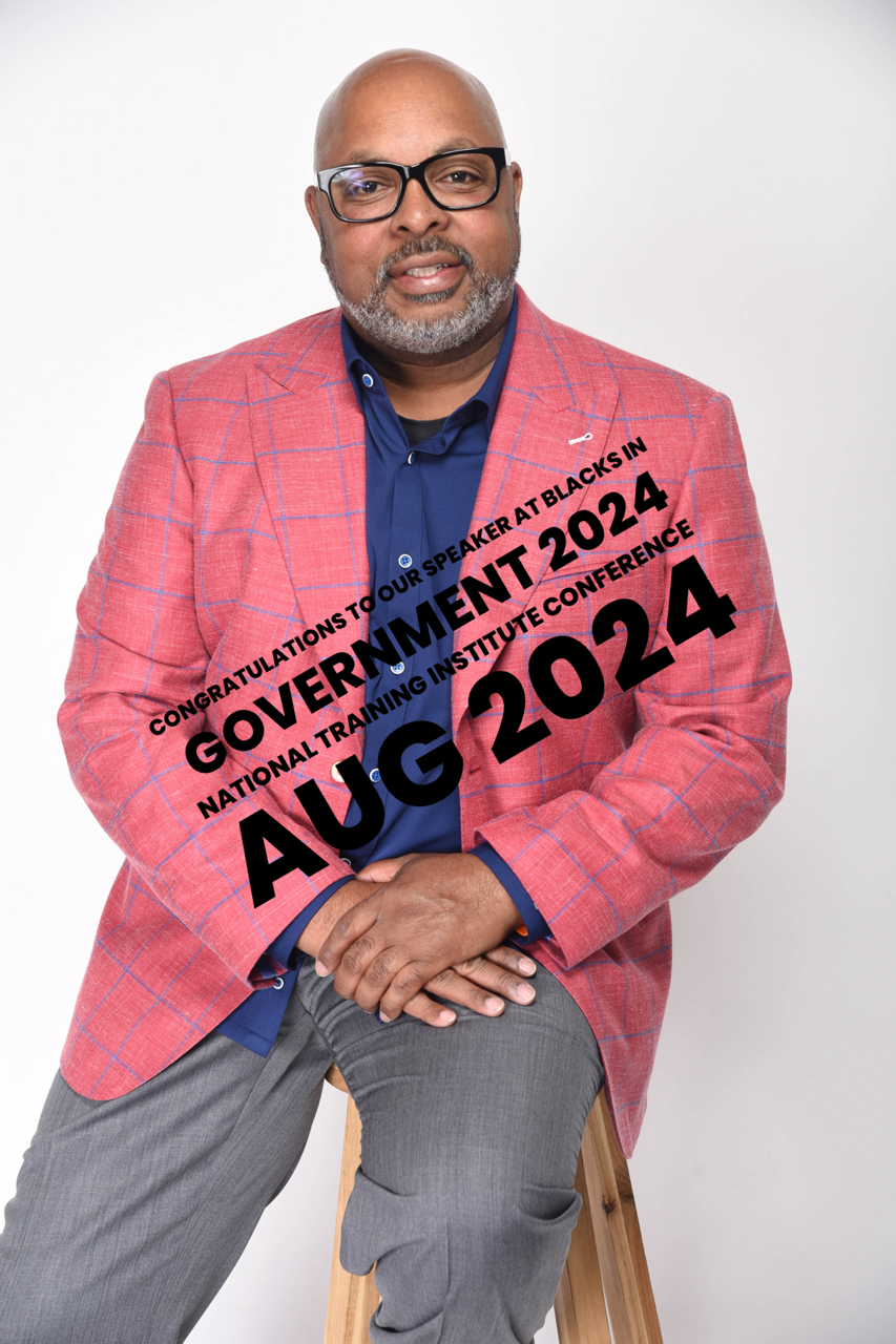 A man in a pink jacket and glasses is sitting on a stool.