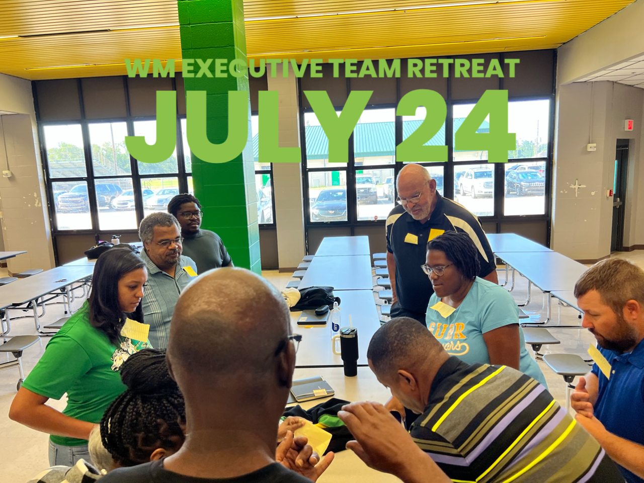 A group of people are gathered around a table with a sign that says wm executive team retreat july 24
