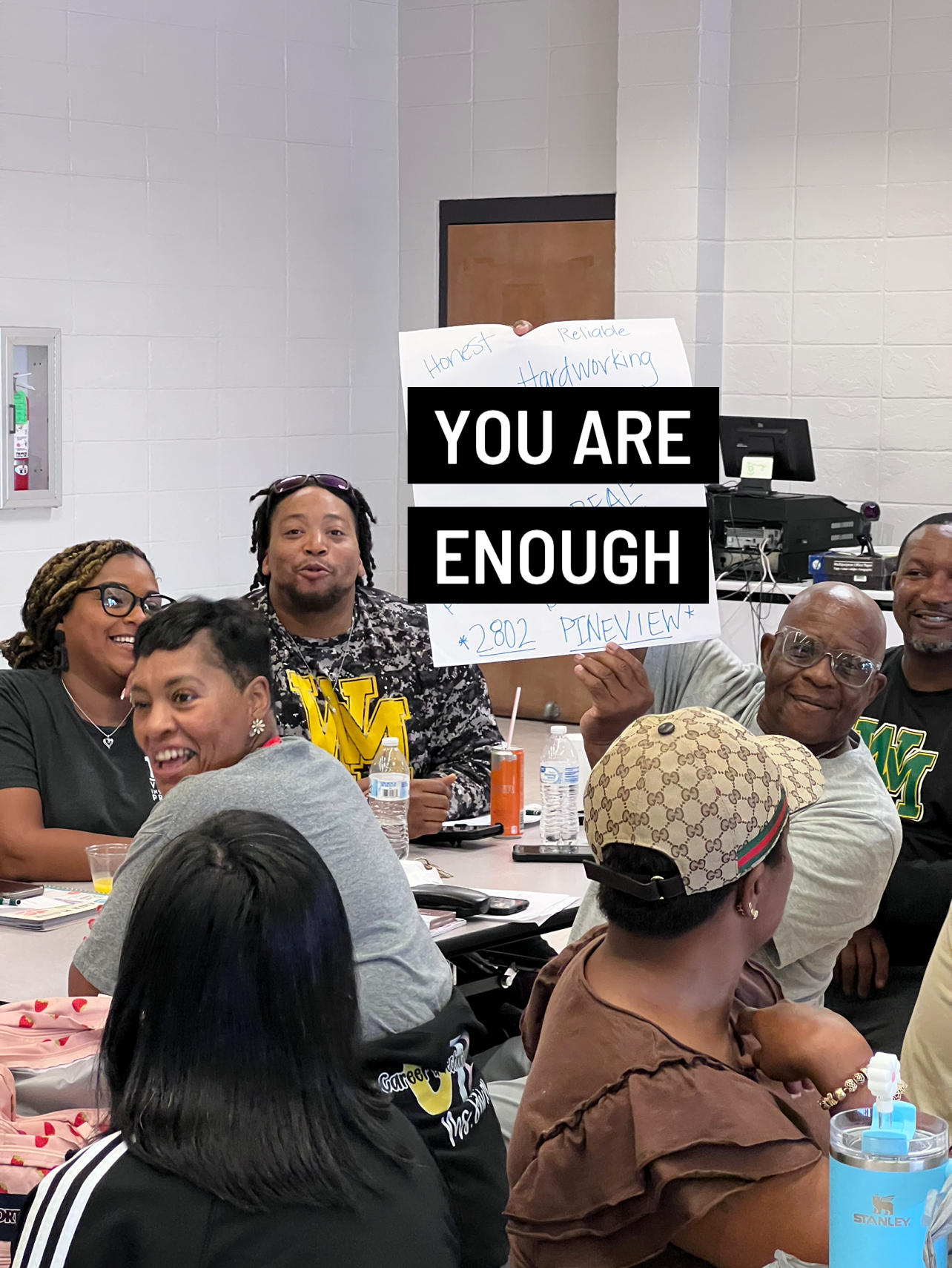 A group of people are sitting around a table with a sign that says `` you are enough ''.